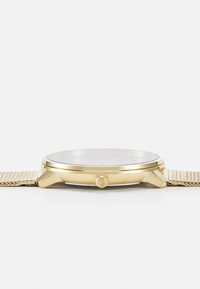 Reloj de metal dorado con una caja redonda, una superficie de cristal suave y una pulsera de malla con un patrón texturizado. Contador lateral para ajustar la hora.