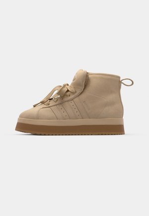 Beige suède high-top sneakers met een dikke rubberen zool, voorzien van een opvouwbare tong, ronde neus en decoratieve veters.