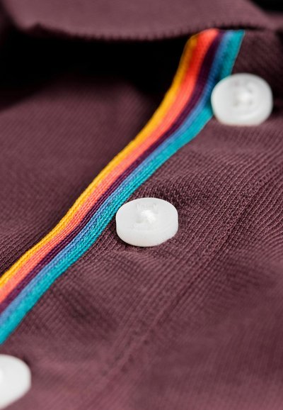 Camicia di un viola scuro con tessuto texturizzato, bottoni bianchi e una striscia multicolore di rosso, giallo e blu al centro.