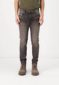Gray denim jeans with a slim fit, featuring a faded finish, five pockets, and contrasting stitching, paired with brown suede boots.