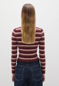 Top de manga larga de rayas burdeos con canalé, con rayas rosas y blanco roto, combinado con jeans oscuros de tiro alto que presentan discretos bolsillos traseros.