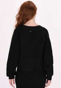 Maglione nero in tinta unita con texture a coste, maniche larghe e vestibilità corta. Presenta un piccolo etichetta con logo sul retro e polsini a maglia.