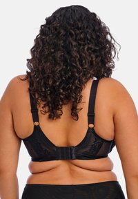 Černé spodní prádlo s krajkovými detaily, nastavitelné ramínka a uzavírání na háček a oko. Zadní část má hladkou tkaninu a ozdobné prvky.