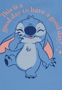 Camiseta de color azul claro con un personaje de dibujos animados con grandes orejas, sonriendo y guiñando un ojo, con texto en rosa que dice "¡Hoy es un buen día para tener un buen día!"