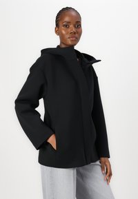 Black hooded jacket made of smooth fabric, featuring a relaxed fit, front pockets, and a minimalistic design with no visible fastenings.