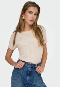 Beżowy prążkowany sweter z krótkim rękawem w połączeniu z dżinsowymi spodniami w kolorze niebieskim o wysokim stanie. Tekstura wydaje się miękka; sweter ma okrągły dekolt i dopasowany krój.