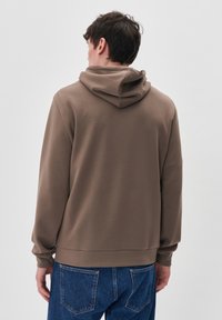 Sudadera con capucha marrón hecha de una tela suave, con un corte relajado y puños acanalados. Se pueden ver los jeans azules a la altura de la cintura.
