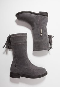 Bottes en suede grises mi-mollet avec des semelles noires, fermeture éclair sur une botte et franges décoratives à l'arrière.