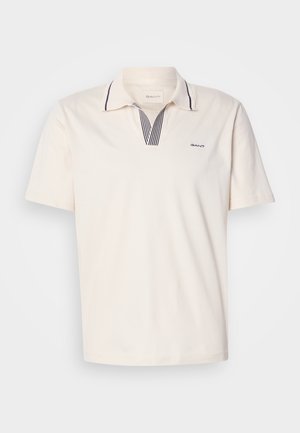 Kreminė polo marškinė su V formos iškirpte, turinčiais mėlynas ir baltas dryžuotas akcentus, trumpomis rankovėmis ir mažu logotipu kairėje krūtinės pusėje.