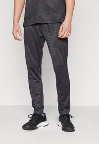 Zwarte sportbroek met een getextureerd, geometrisch patroon, met een slim fit en elastische tailleband, gecombineerd met zwarte sneakers.