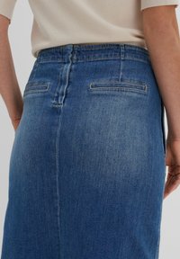 Jupe en denim bleu moyen avec une silhouette ajustée, dotée de deux poches arrière et d'un léger délavage près de l'ourlet, avec des coutures renforcées.