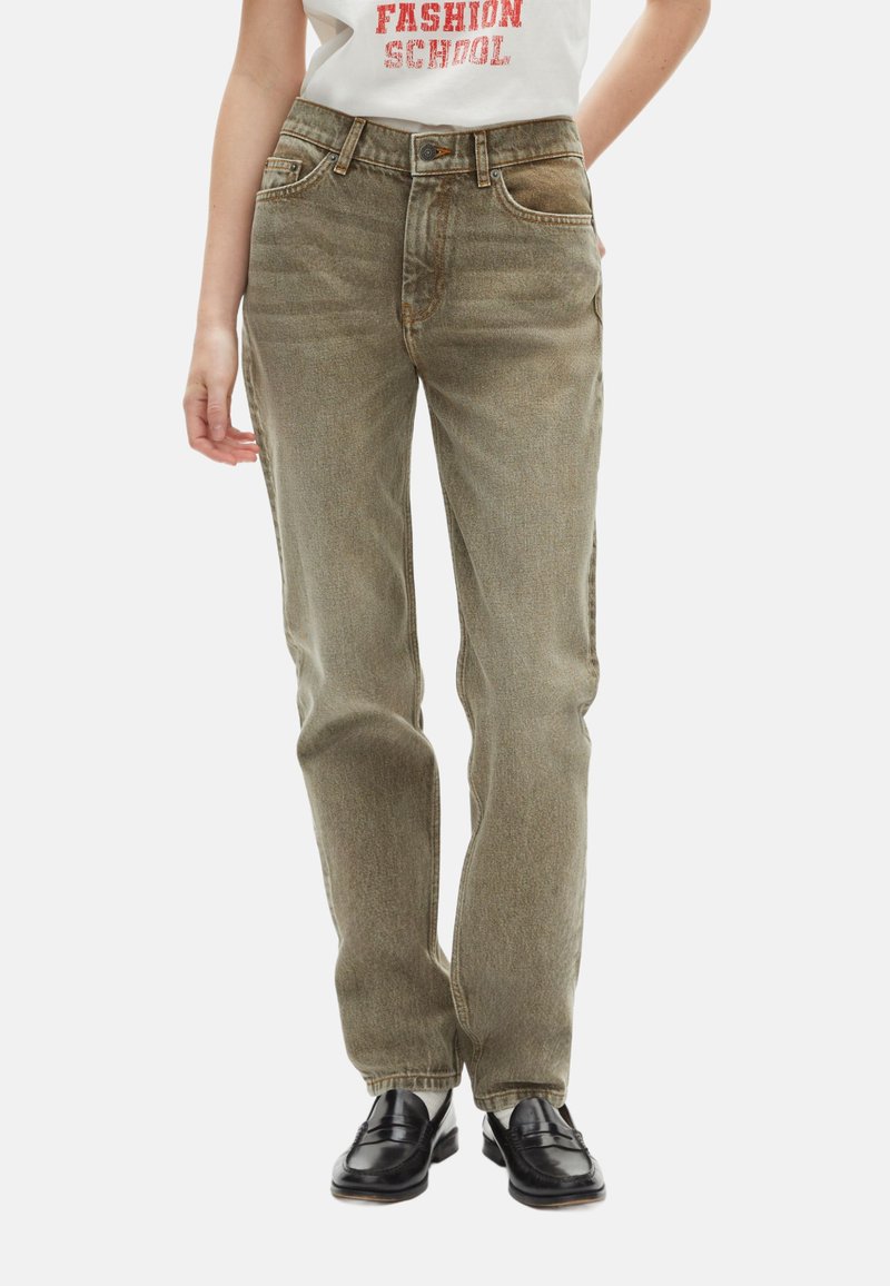 Jeans de mezclilla verde claro con un corte recto, cinco bolsillos y costuras de cobre. Combinados con mocasines negros y una camiseta gráfica blanca.