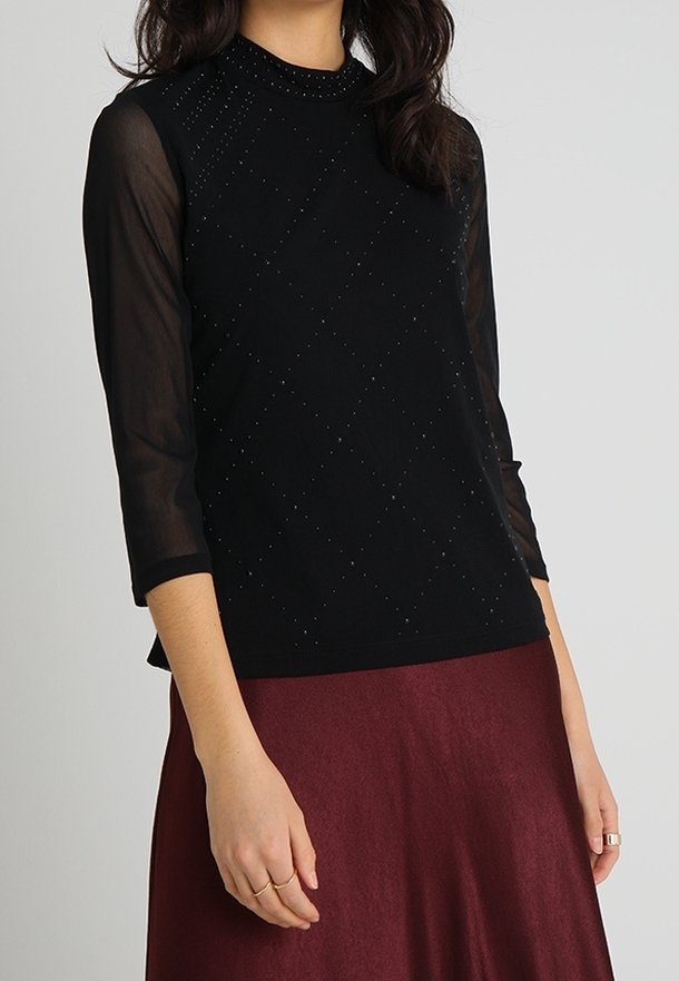 Haut noir avec un motif en losanges texturé et des accents scintillants. Manches noires transparentes, encolure ronde, associé à une jupe bordeaux.