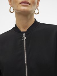 Priročni posnetek osebe, ki nosi zlate obroče in črn jopič z zadrgo, ki ima kroglo za vlakanje.