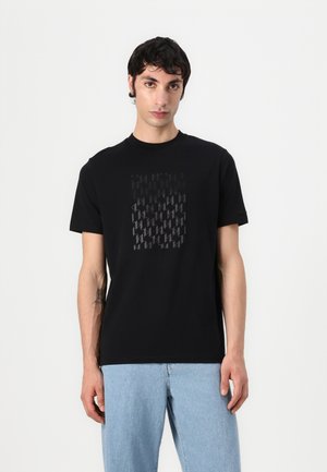 Svart bomull t-skjorte med et geometrisk tonalt mønster i midten. Korte ermer og rund halsdesign. Kombinert med lyseblå jeans.