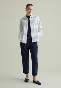 Camicia a righe bianca e blu navy, indossata sopra un top blu navy, abbinata a pantaloni blu navy e ballerine blu navy. Tessuto morbido, vestibilità rilassata.