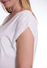 Witte katoenen T-shirt met een V-hals, korte mouwen en subtiele plooien bij de schoudernaad. Gladde structuur en casual pasvorm.