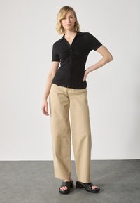 Black short-sleeved top with a front twist detail, paired with beige wide-legged pants and black platform sandals. Light gray background.
