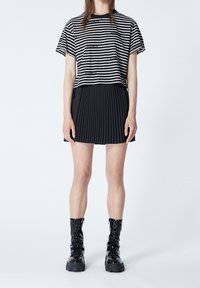 Svartvit randig kortärmad topp i kombination med en svart plisserad kjol och svarta snörda platåstövlar. Släta texturer genom hela outfiten.