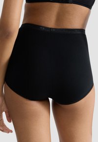 Czarne majtki z wysokim stanem wykonane z miękkiego materiału, z falistą elastyczną gumką w pasie, zapewniające pełne krycie i gładkie wykończenie.