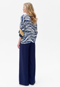 Luźna bluzka w białym kolorze z niebieskimi wzorami liści i żółtymi akcentami, połączona z szerokimi granatowymi spodniami. Miękka tekstura, luźny krój i krótkie rękawy.