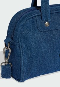 Blå denim axelväska med rundad form, dragkedjestängning, dubbla handtag och metallspänne. Har synliga sömmar och en accentlogotyp.