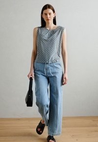 Ermeløs mønstrete bluse i svart og hvitt, sammen med lyseblå vide jeans. Svart veske og sandaler fullfører antrekket.