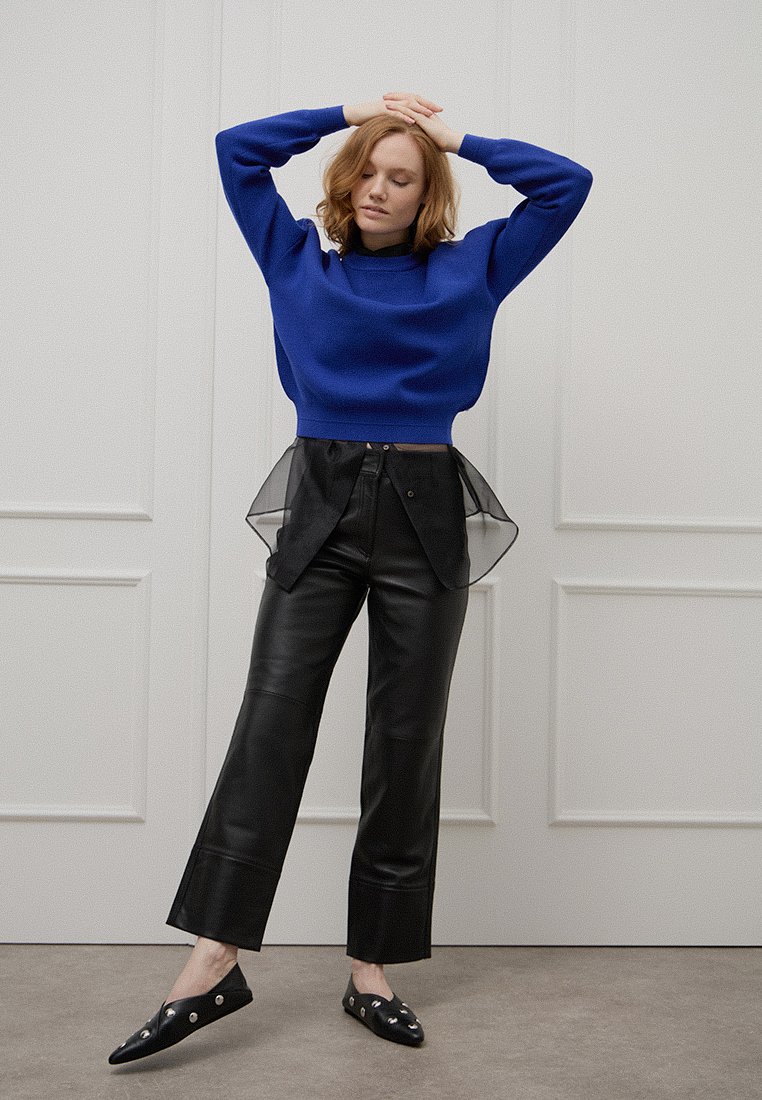 Niebieski sweter z dzianiny, czarne skórzane spodnie z siatkowym nałożeniem i czarne mokasyny ze srebrnymi akcentami. Prosty, współczesny design.