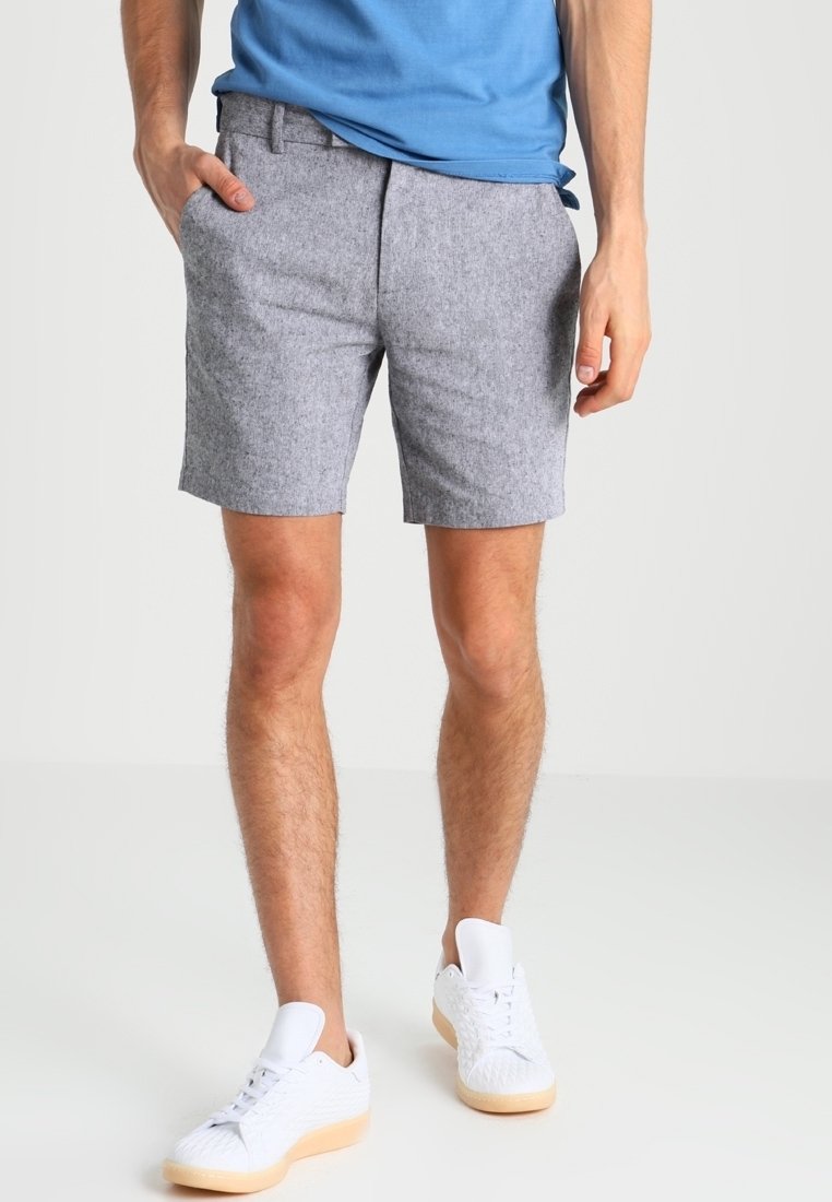 Shorts gris texturés avec poches avant et coupe droite, associés à des baskets blanches et une chemise bleue. Design simple, palette neutre.