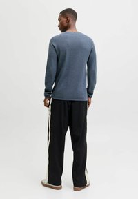 Blå genser med lange ermer og teksturert overflate, kombinert med svarte bukser med kremfargede sidestriper og brune joggesko.