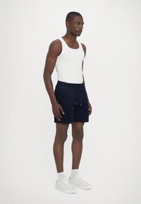 Shorts bleu marine avec taille élastique et cordon de serrage, associés à un débardeur blanc et à des sneakers blancs. Tissu lisse et coupe décontractée.
