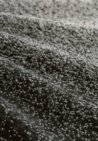 Strickstoff in Grau- und Schwarztönen mit einer strukturierten, gemusterten Webart. Weiche, leicht erhabene Textur mit kontrastierenden Sprenkeln durchgehend.