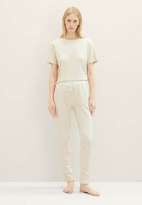 Haut à manches courtes beige clair associé à un pantalon de jogging beige à motifs présentant des designs géométriques. Tissu doux et taille élastique visibles.