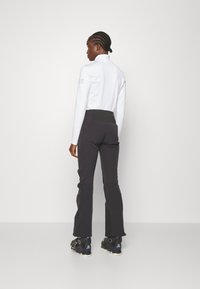 Witte hoge hals top met lange mouwen en zwarte fitted broek. De broek heeft een zwarte tailleband en uitlopende onderkant. Zwarte schoenen met paarse accenten.