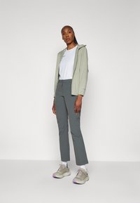 Lys grøn zip-up hettegenser, hvit t-skjorte, grå bukser og beige sneakers med lilla detaljer. Glatt stoff, tettsittende design og praktisk form.