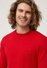 Maglione rosso a maglia con scollatura rotonda e maniche lunghe, caratterizzato da un piccolo logo ricamato di colore contrastante sul petto.