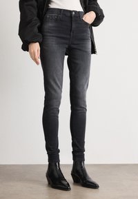 Fekete, magas derekú, skinny farmernadrág, elhalványult mosással, szoros fazonnal és enyhe gyűrődés részletekkel. Bokáig érő csizma, bootcut stílusban.