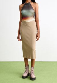 Top de cuello halter con colores degradados que van del verde al naranja, combinado con una falda midi de punto beige y botas rosas con cordones.