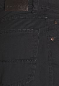 Jeans in denim nero con tessuto testurizzato, design a cinque tasche, toppe in pelle marrone e cuciture a contrasto. Inclusi accessori in metallo.
