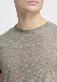 Grå-brun kortærmet t-shirt med en subtil tekstur og rund hals. Stoflet indeholder et meleret mønster med fine linjer.