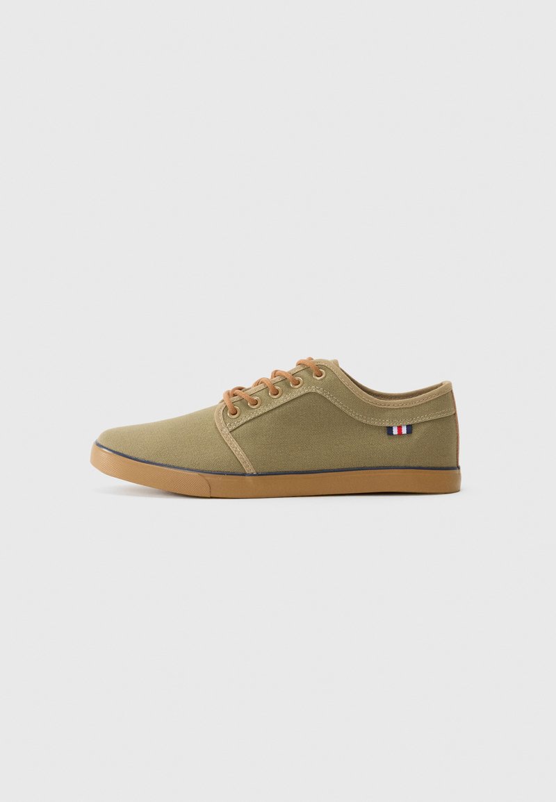 Olive green canvas sneaker with brown laces and rubber sole, featuring a small tri-color accent near the heel and a low-top design.