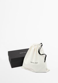 Sacchetto in cotone con coulisse di colore crema e dettagli neri, affiancato da una scatola rettangolare nera con il logo "Massimo Dutti" in bianco.