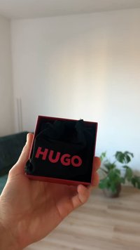 Boîte cadeau rouge avec un intérieur noir affichant une pochette noire. Le mot « HUGO » est embossé en rouge vif sur le devant de la boîte.