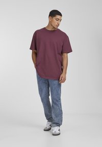 Burgundi színű, oversized póló, pamut szövetből készült, kerek nyakkivágással, világoskék denim farmernadrággal párosítva, amely egyenes szabású és enyhén kopott.