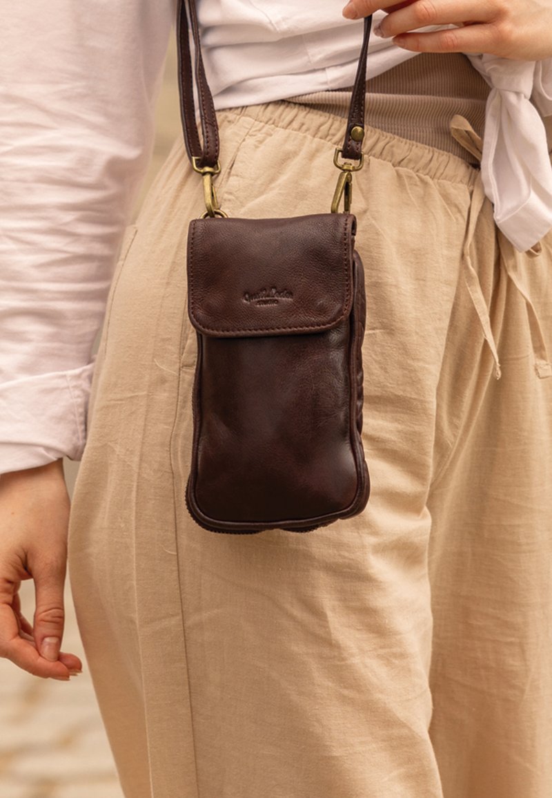 Borsa a tracolla in pelle marrone con chiusura a patta, caratterizzata da una texture liscia e da un branding sottile, sospesa da una tracolla in ottone.