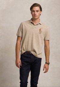 Beige színű polo ing gallérral, az mellrészen egy hímzett barna ló logóval, sötétkék farmernadrággal párosítva.
