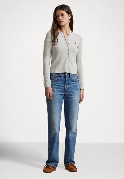 Γκρι μακρυμάνικο πουκάμισο με κουμπιά, στρογγυλή λαιμόκοψη και στενή εφαρμογή, συνδυασμένο με ανοιχτό μπλε τζιν παντελόνι με ίσια μπατζάκια και καφέ μοκασίνια με κορδόνια.