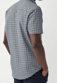 Camisa de manga corta a cuadros en azul marino y blanco, fabricada con tela tejida, que presenta un corte relajado y un dobladillo redondeado.