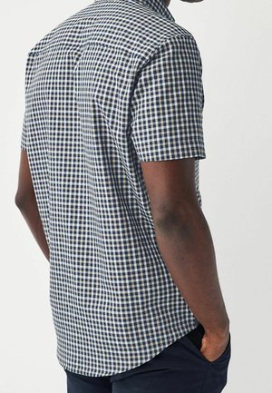 Koszula w kratę z krótkim rękawem w kolorze granatowym i białym, wykonana z tkaniny o splocie, charakteryzująca się luźnym krojem i zaokrąglonym dolnym brzegiem.
