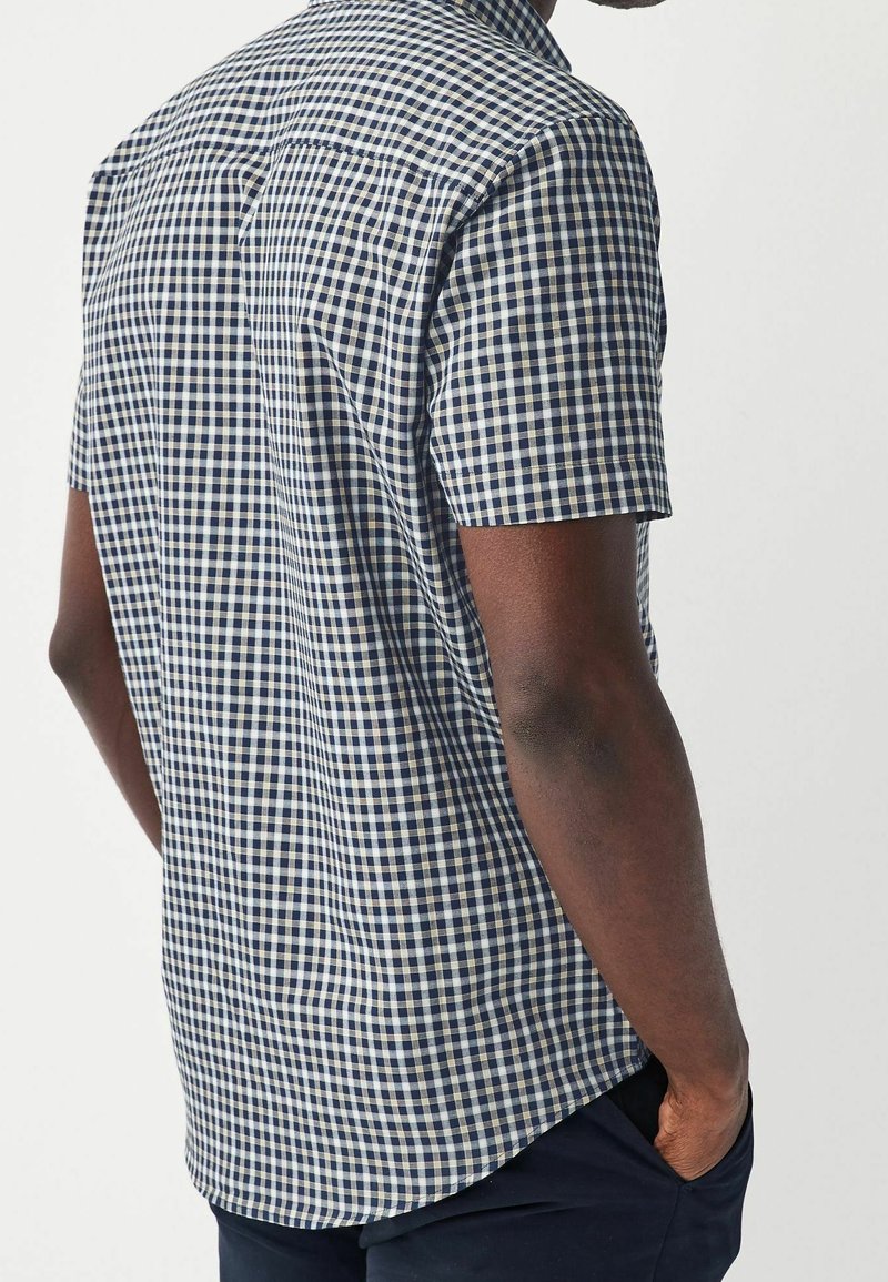 Camisa de manga corta a cuadros en azul marino y blanco, fabricada con tela tejida, que presenta un corte relajado y un dobladillo redondeado.